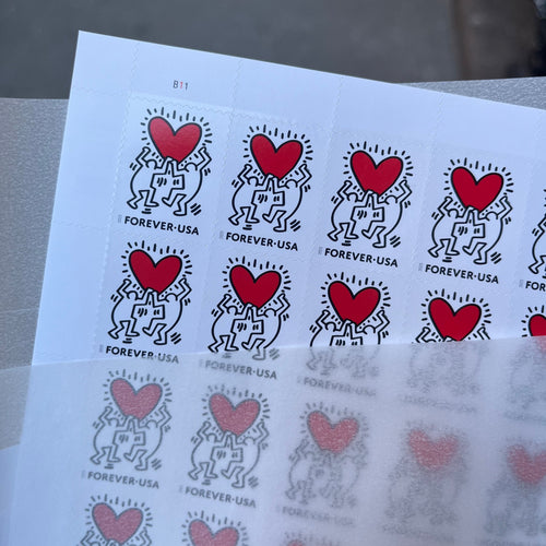 Sheet of postage stamps with red hearts and black designs on a white background.